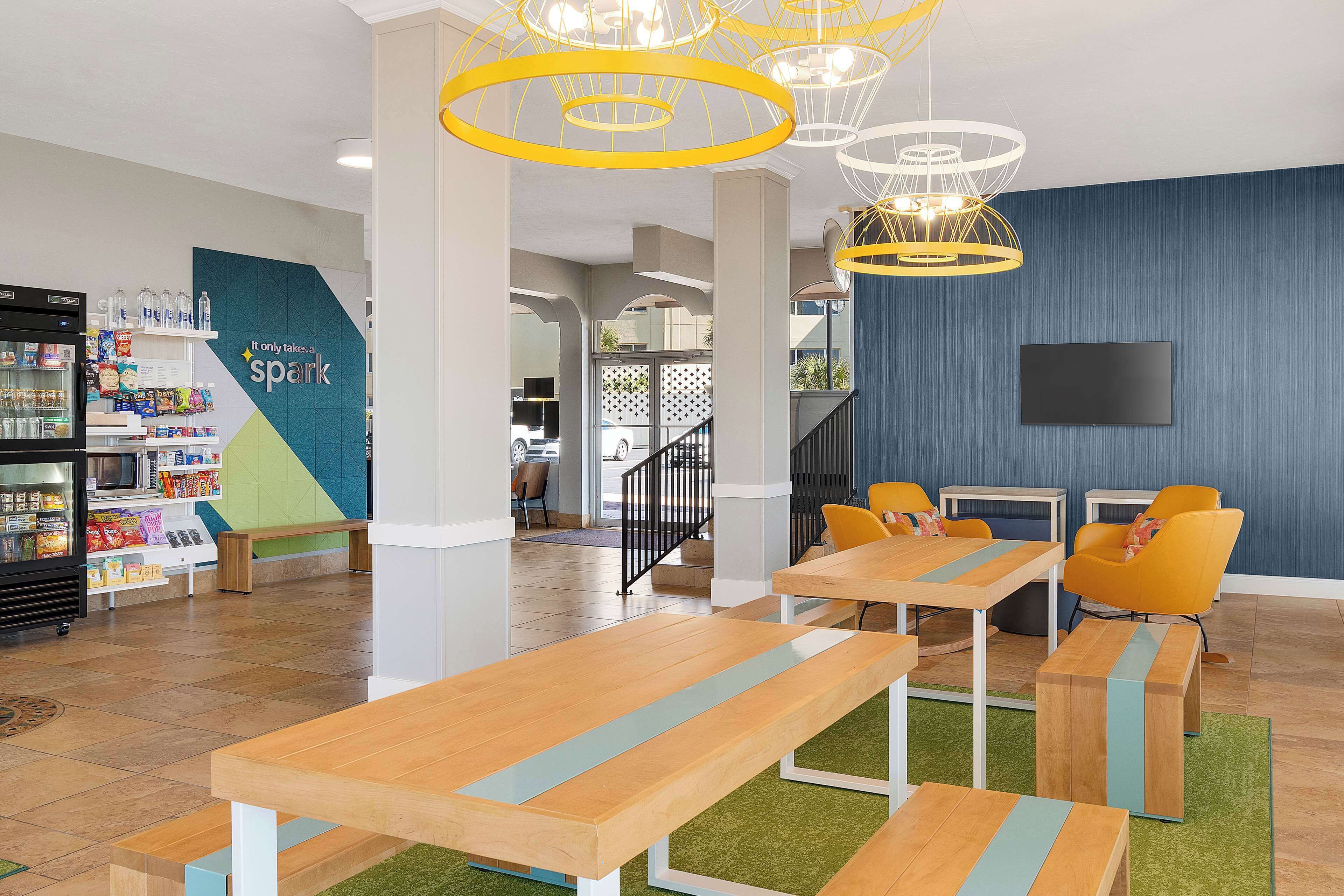 A modern indoor space with wooden tables and benches, a vending machine, and a wall-mounted TV.
