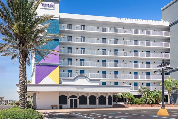A multi-story hotel with a white facade, blue balconies, and a parking lot with marked spaces. - Spark by Hilton Ormond Beach Oceanfront (Ormond Beach)