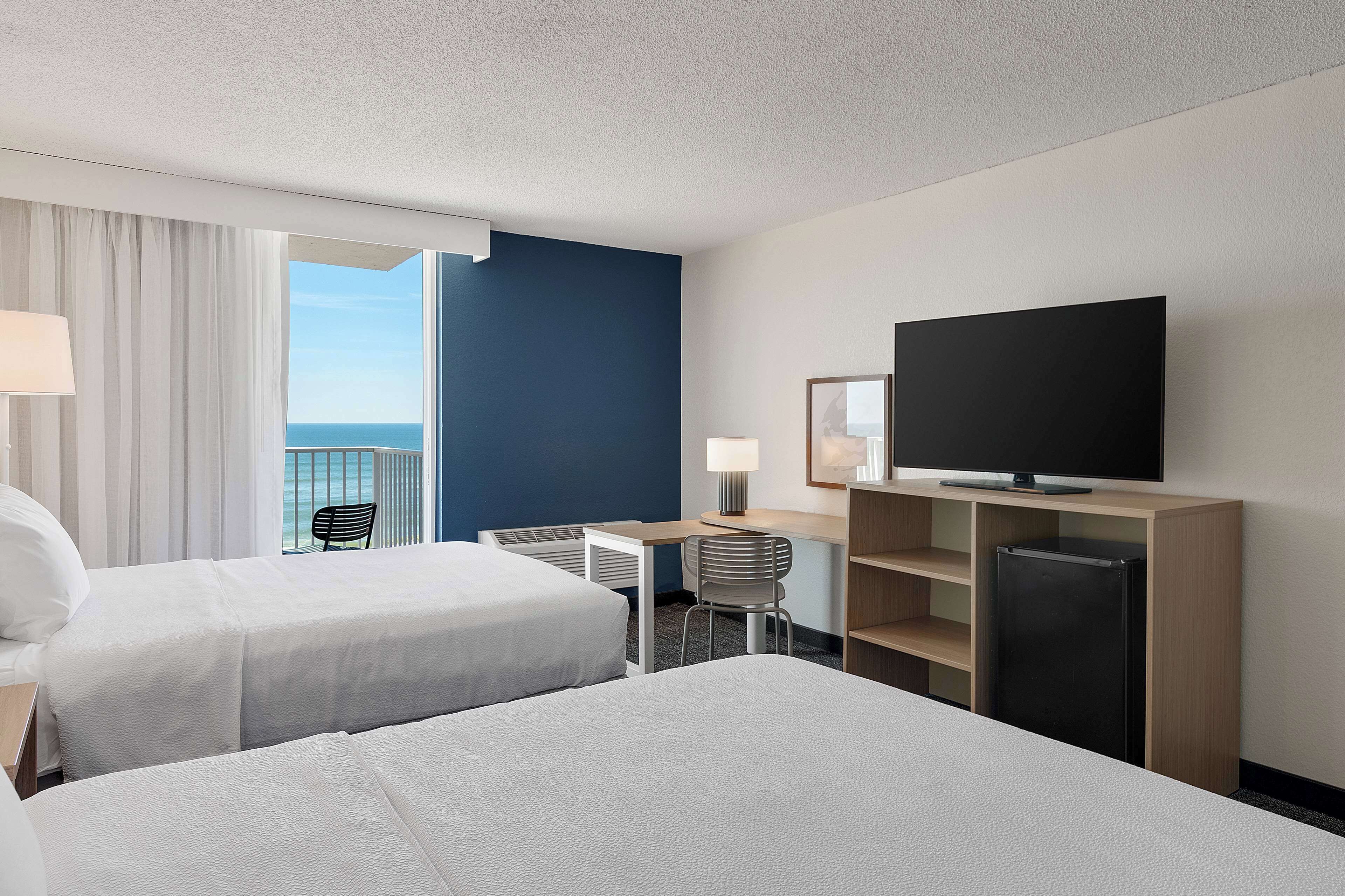 Habitación de hotel con dos camas, un escritorio, una silla, un televisor y vista al océano.