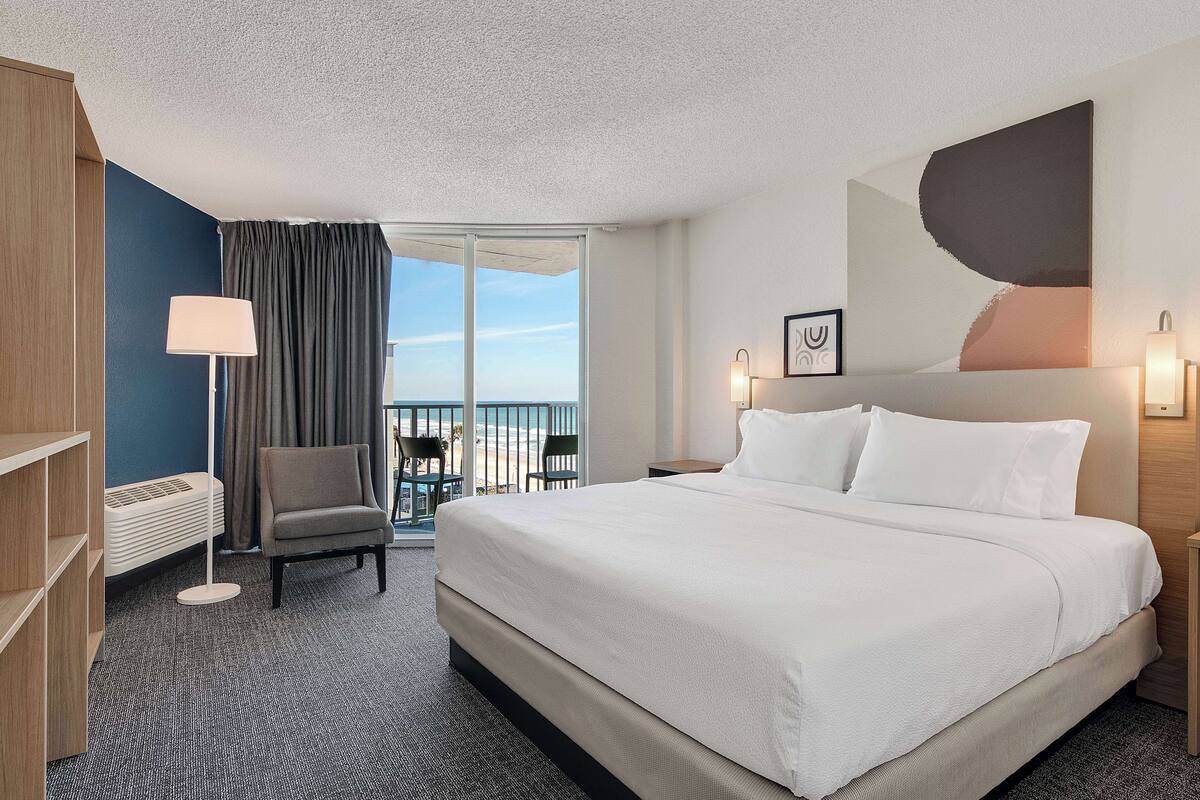 Habitación de hotel con una cama grande, una silla, un escritorio y vistas al exterior.