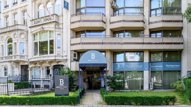 En bygning med flere etager og en moderne indgang, hvor der står "B Apart Hotels".
