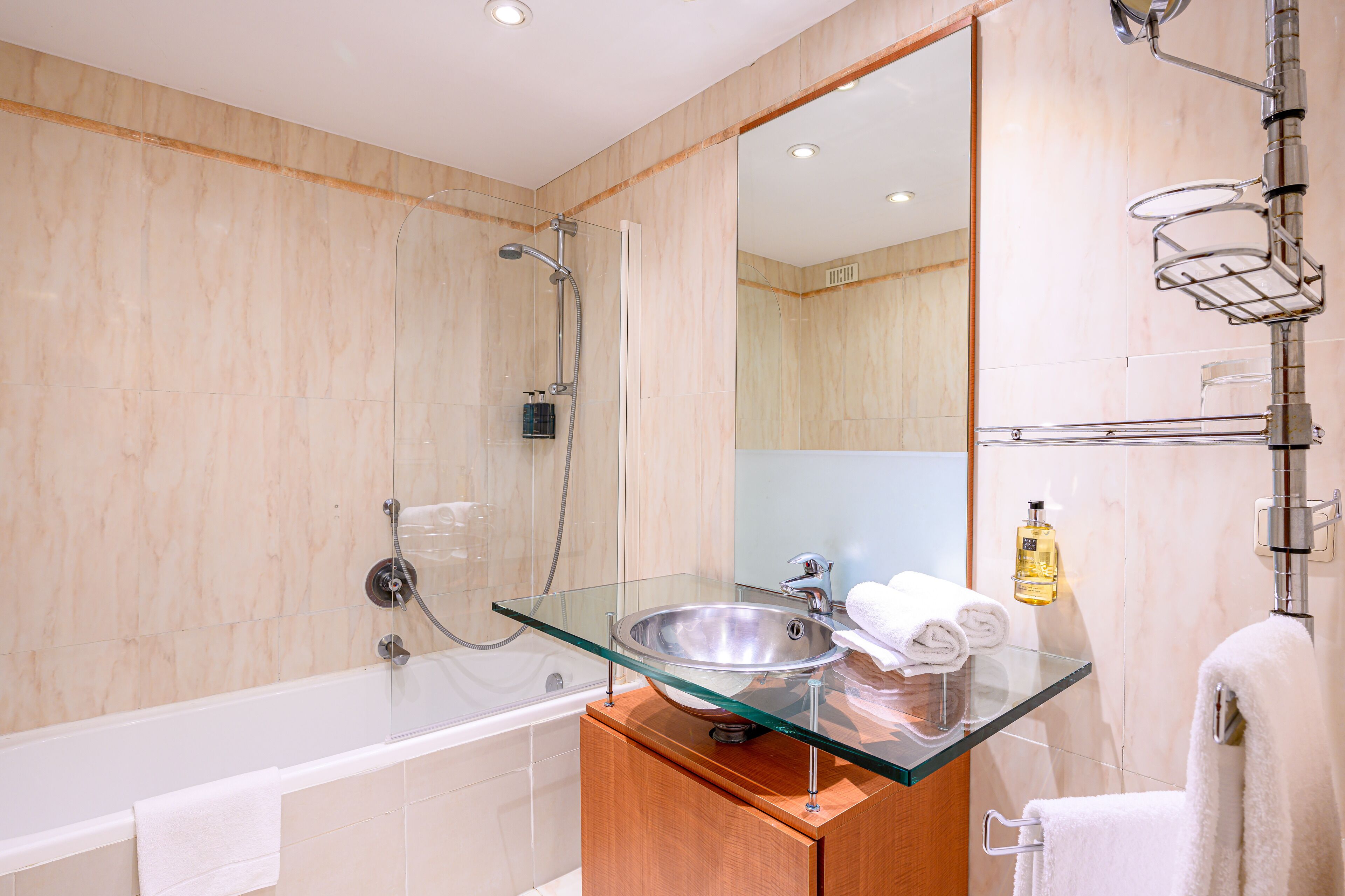 A modern bathroom with a glass-enclosed sink, a bathtub, and a large mirror.