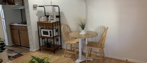 A compact living space with a kitchenette, a dining area with a table and chairs, a TV mounted on the wall, and a potted plant on the floor.