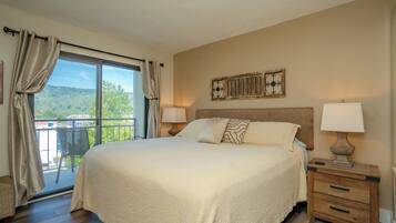 A hotel room with a large bed, two bedside tables with lamps, a view of the outdoors, and a decorative wall piece.