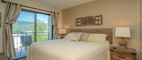 A hotel room with a large bed, two bedside tables with lamps, a view of the outdoors, and a decorative wall piece.