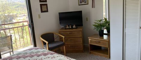 Un dormitorio con cama, televisor, sillón, cómoda y una planta en maceta.