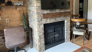 A cozy living room with a stone fireplace, a mounted TV, and a dining area with a round table and chairs. - Laurel Inn Condominium (Gatlinburg)
