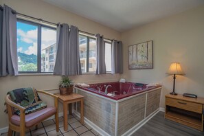 A bathroom with a red bathtub, a wooden chair, a small table, a potted plant, and a painting on the wall. - Laurel Inn Condominium (Gatlinburg)