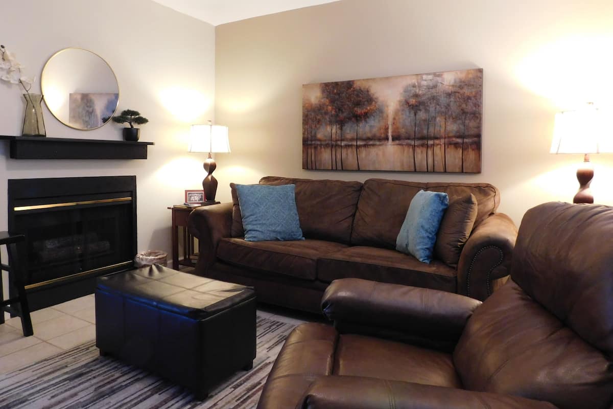 A living room with a fireplace, a brown leather sofa, a coffee table, and a painting on the wall.