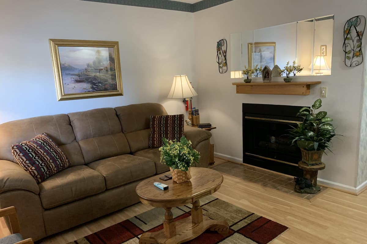 A living room with a brown sofa, a round wooden coffee table, a fireplace, and a painting on the wall.