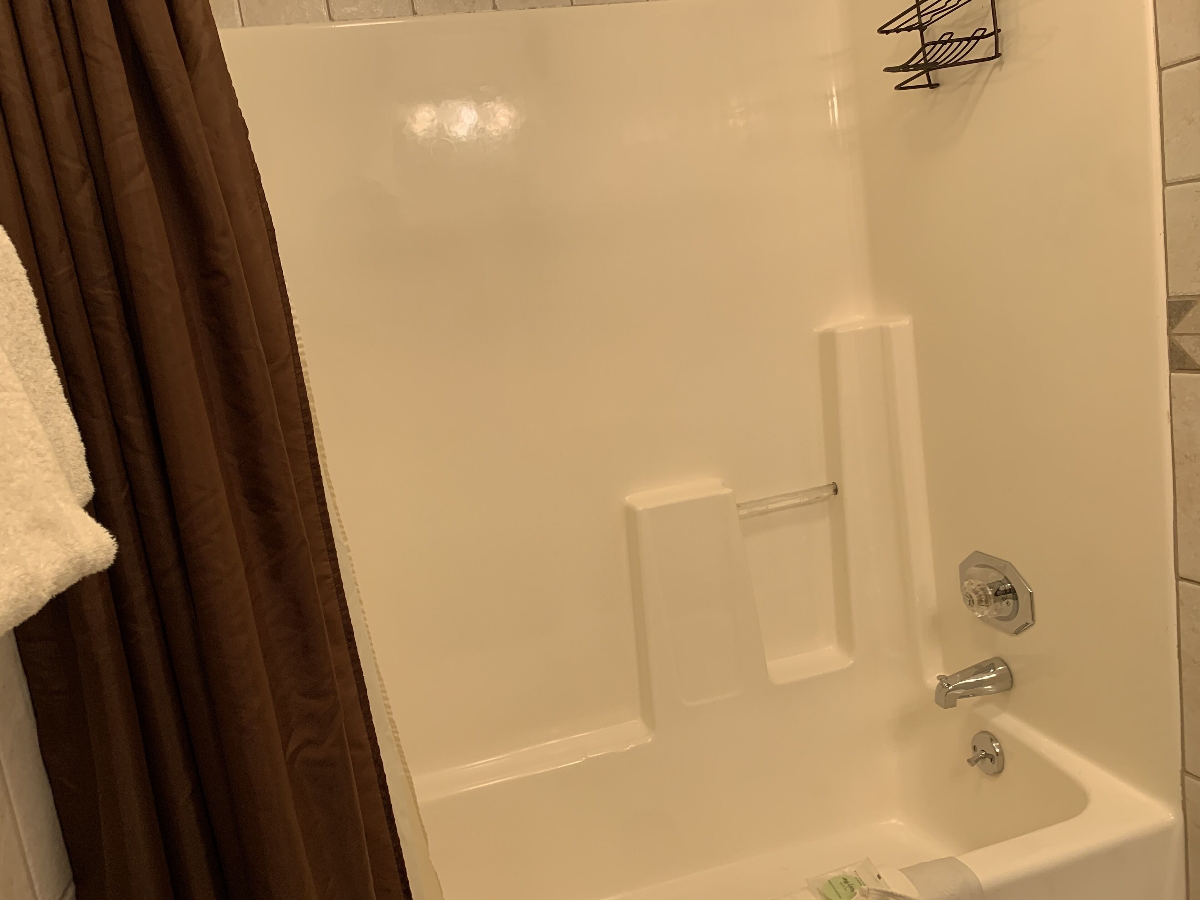 Eine weiße Badewanne mit Duschvorhang, Handtuchhalter und einem kleinen Ablagebrett.