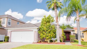 Een woonhuis met een witte garageklep, een rode voordeur en een verzorgd gazon met palmbomen.