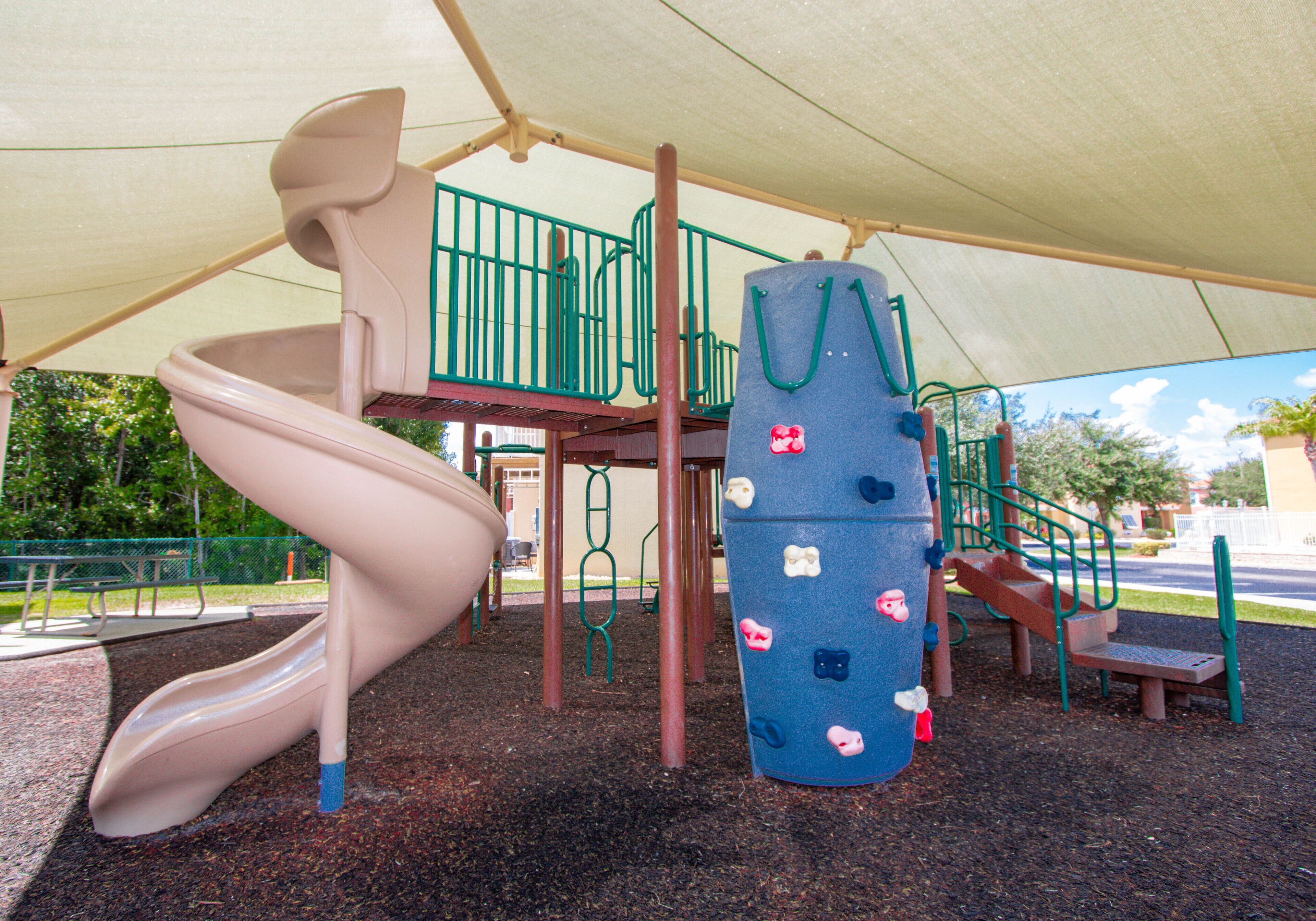 A playground with a slide, climbing structures, and a shaded area.