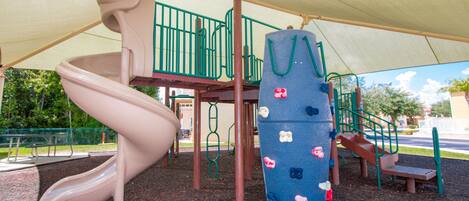 A playground with a slide, climbing structures, and a shaded area.