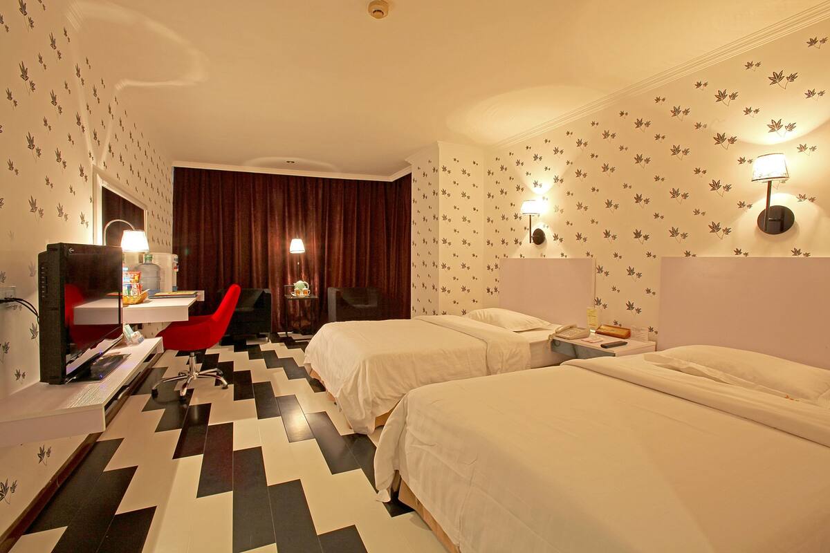 A hotel room with two beds, a desk with a chair, a desk lamp, and a telephone.