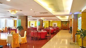 Un amplio salón de banquetes con varias mesas redondas, sillas y un piso pulido.