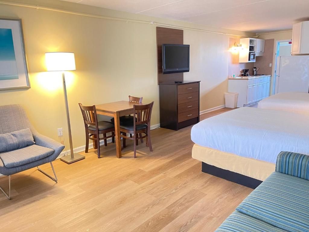 A hotel room with a bed, a desk with a chair, a television, a lamp, and a kitchenette.