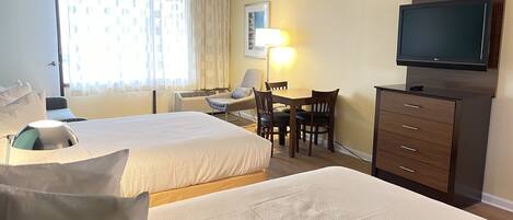 A hotel room with two beds, a desk with chairs, a television, and a lamp.