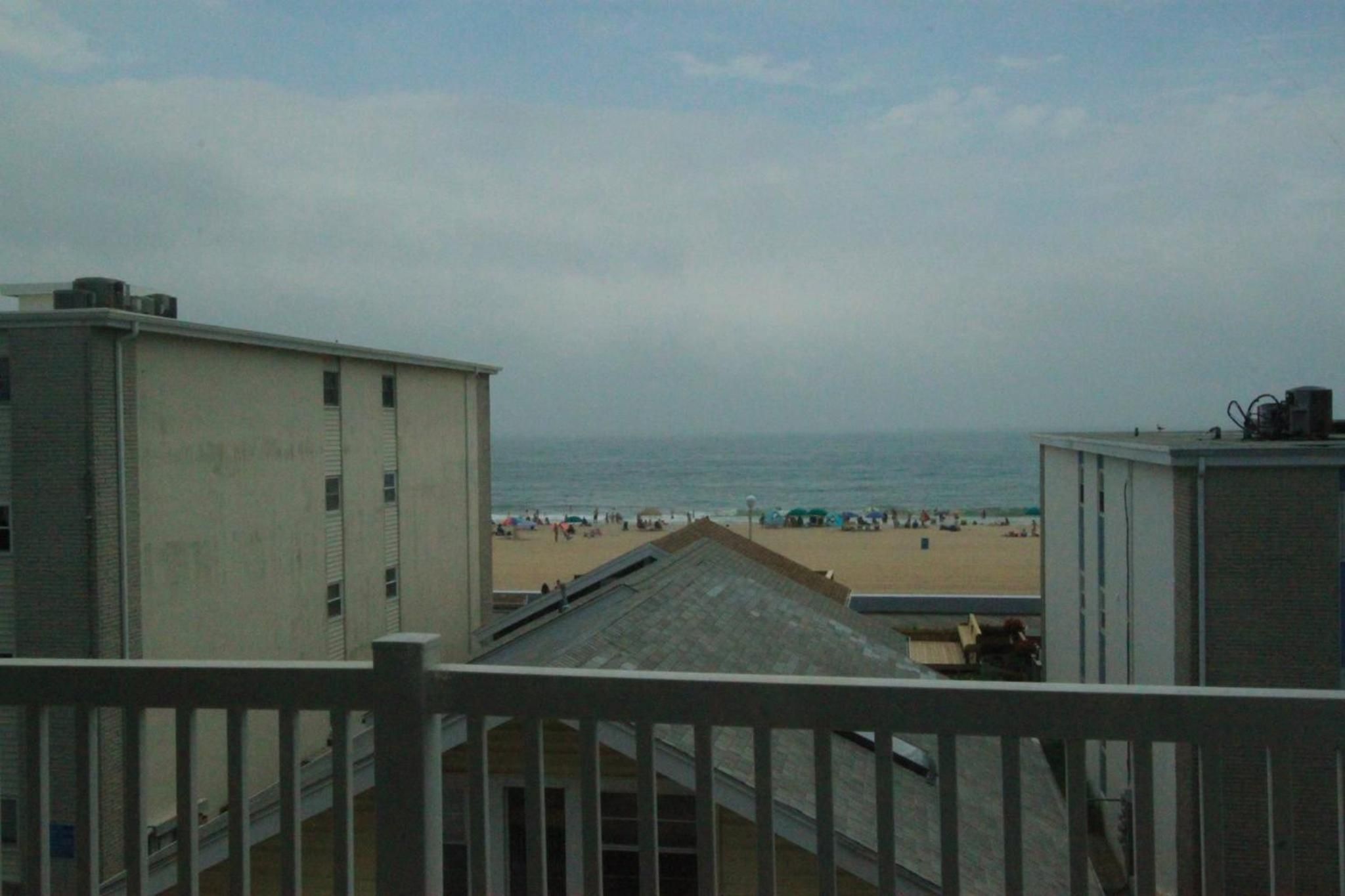 A beach view from a building with a balcony, featuring a sandy beach and the ocean in the background.