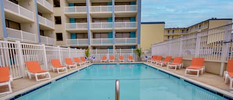 A swimming pool with orange and white lounge chairs, a no diving sign, and a multi-story building in the background.