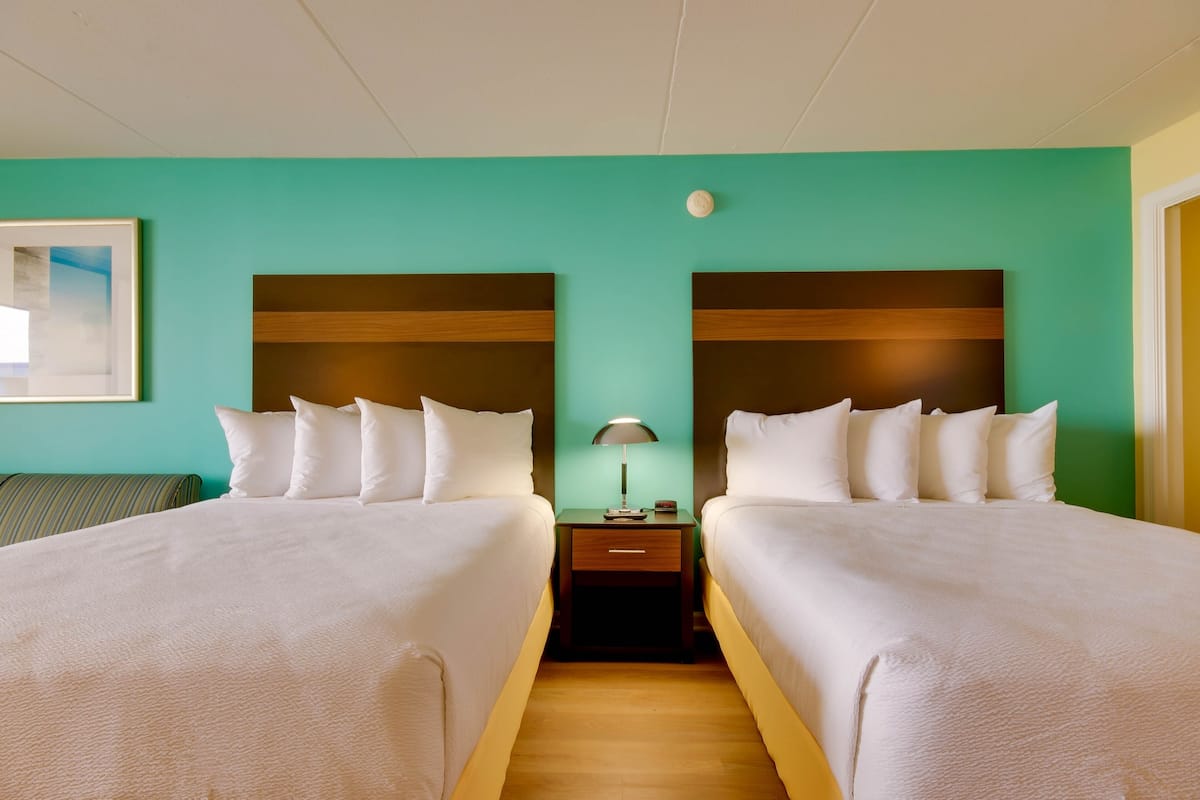 A hotel room with two beds, a nightstand with a lamp, and a green wall.