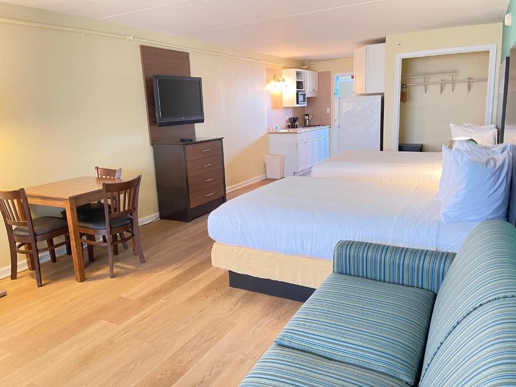 A hotel room with a bed, a sofa, a desk with chairs, a television, a kitchenette, and a bathroom.