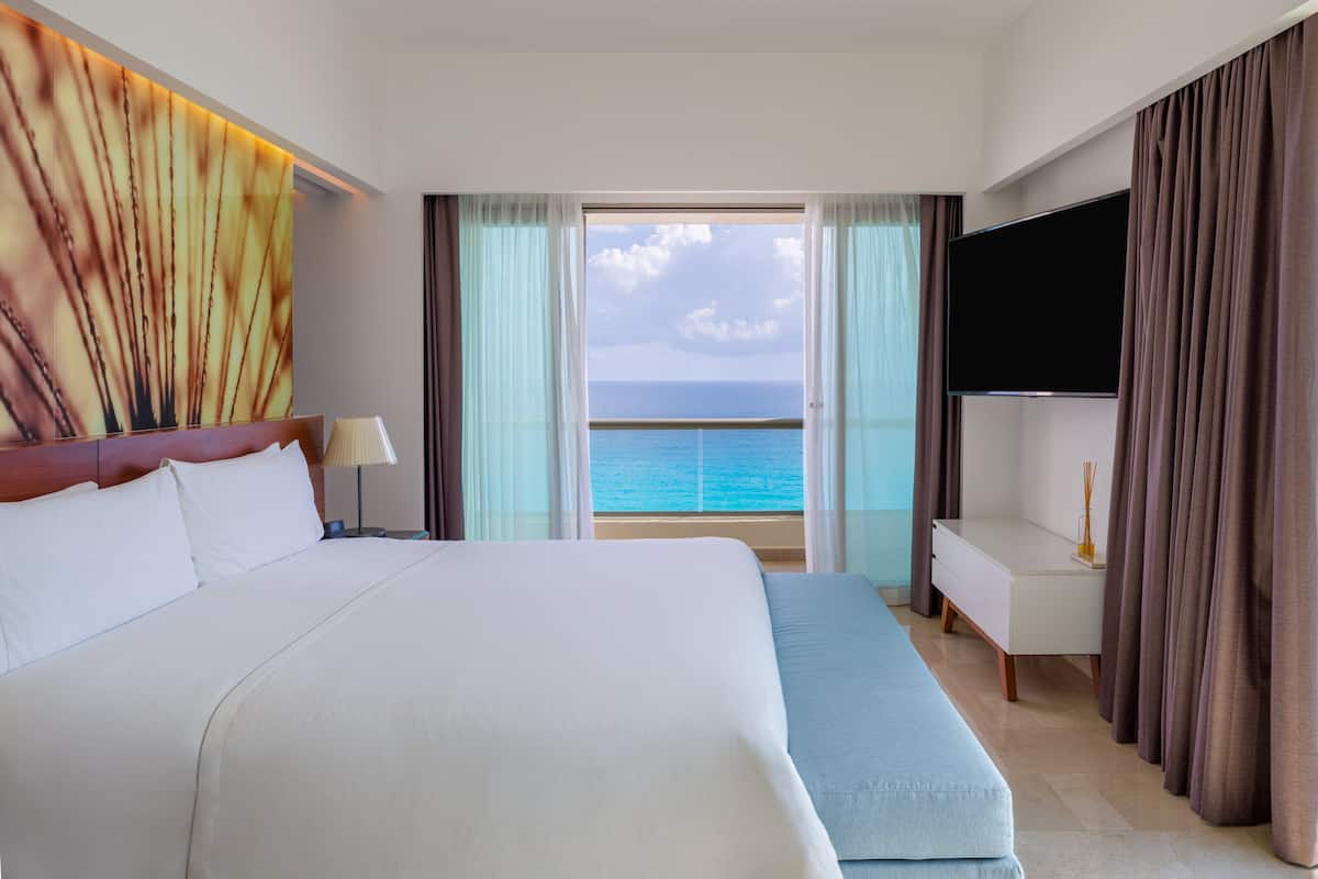 Ein Hotelzimmer mit einem großen Bett, einem Fernseher und Blick auf den Ozean.