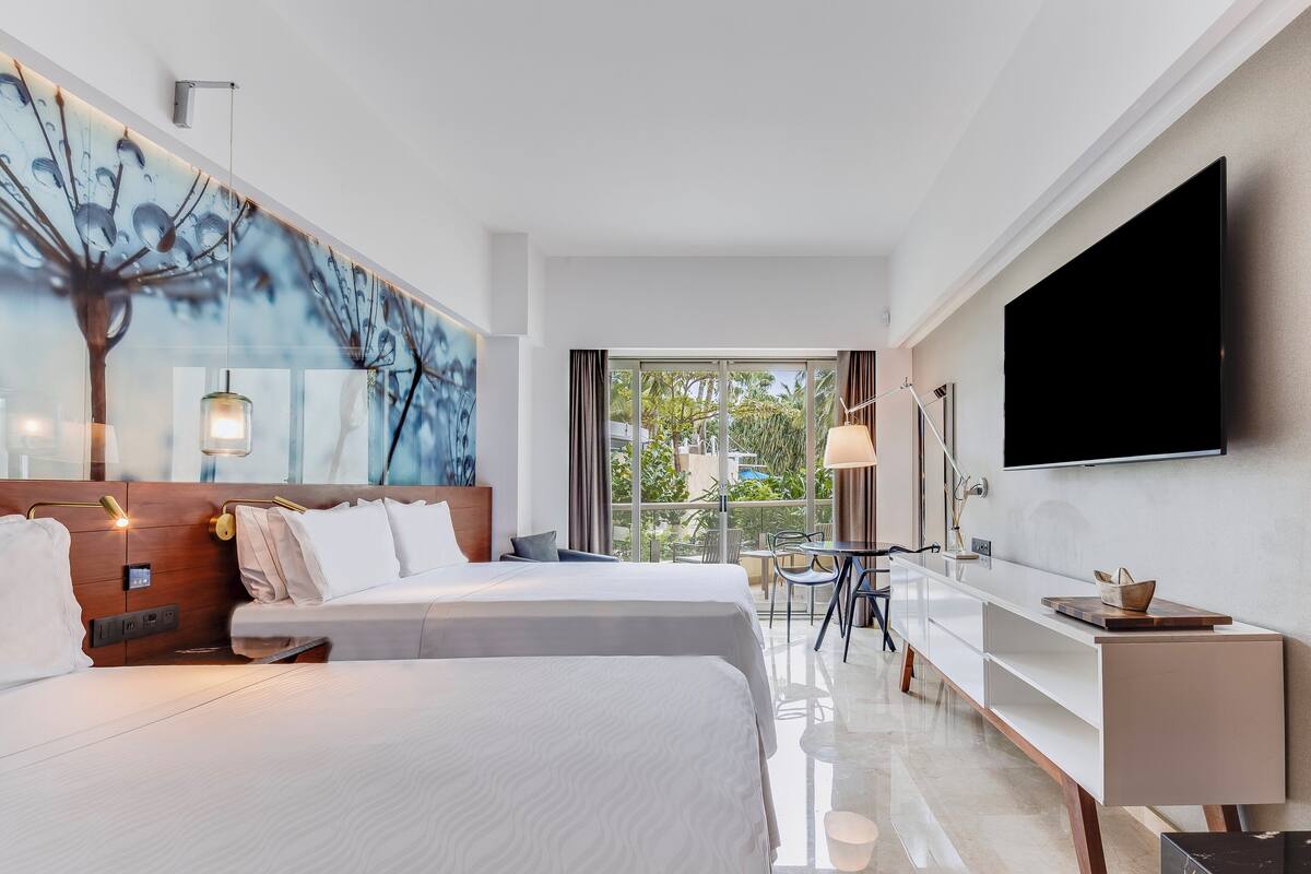 Ein modernes Hotelzimmer mit zwei Betten, einem großen Fenster, einem Flachbildfernseher und einer Essecke.