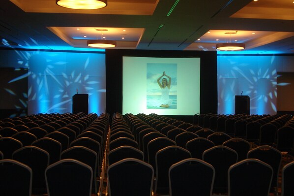 An auditorium with rows of chairs facing a large screen displaying a presentation.