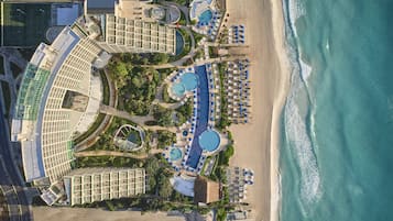 Vista aérea de um resort com várias piscinas, áreas de descanso na praia e um grande complexo de edifícios.