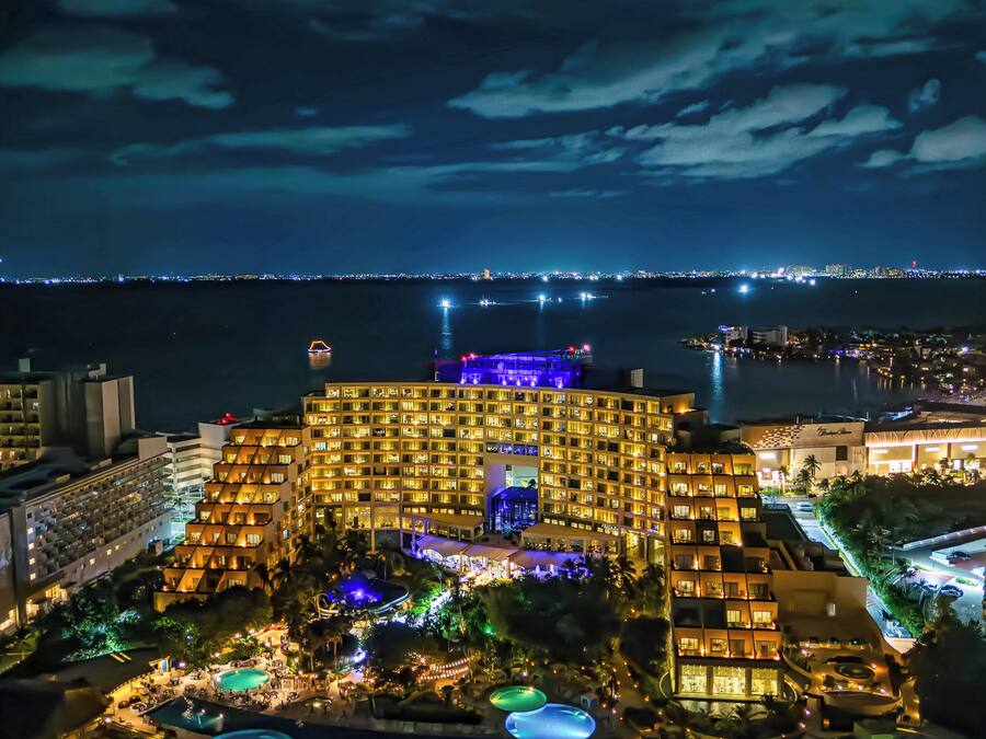 Un gran hotel con varios balcones, un área de piscina y vistas a la silueta urbana nocturna.
