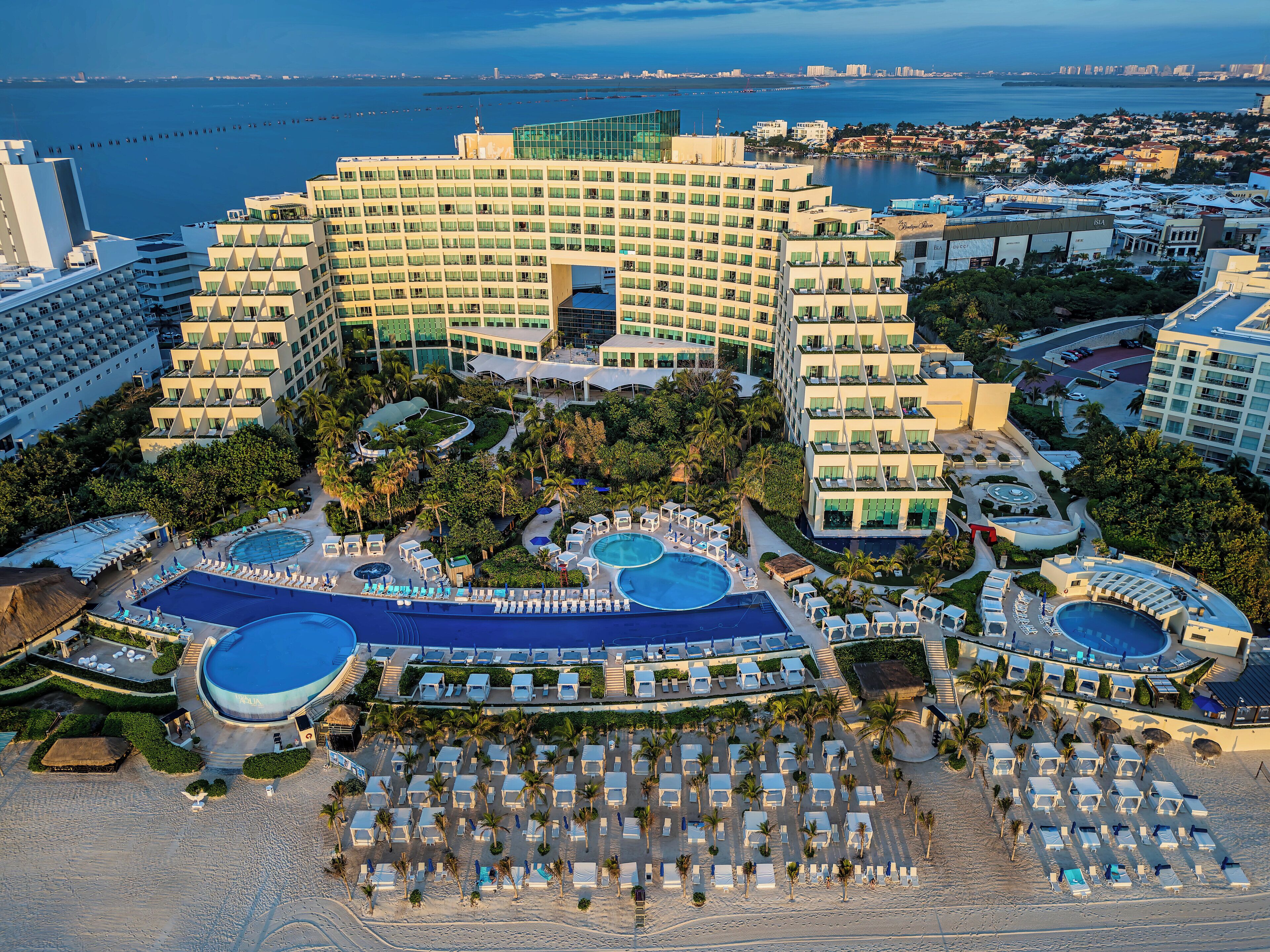 A hotel with multiple swimming pools, a beach area with sun loungers, and a view of the sea.