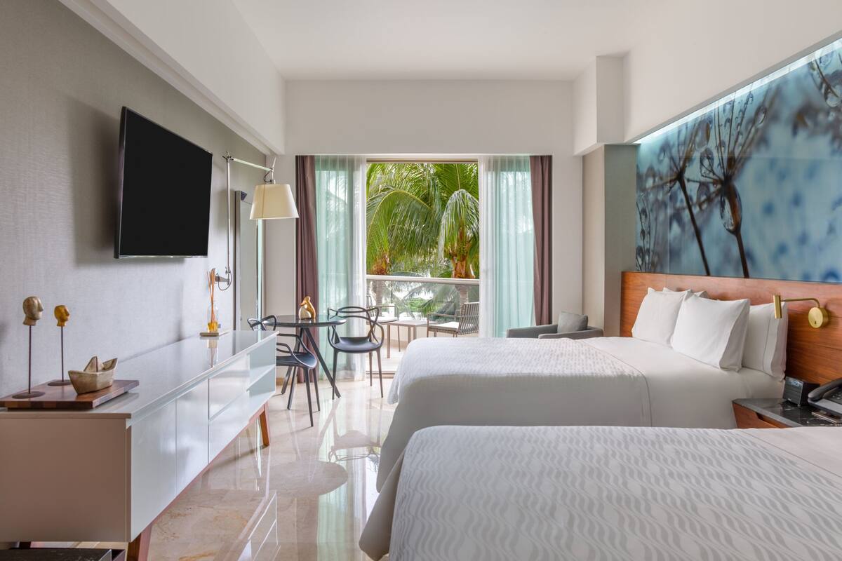 Ein Hotelzimmer mit Bett, Schreibtisch, Sessel, Fernseher und Blick ins Freie.