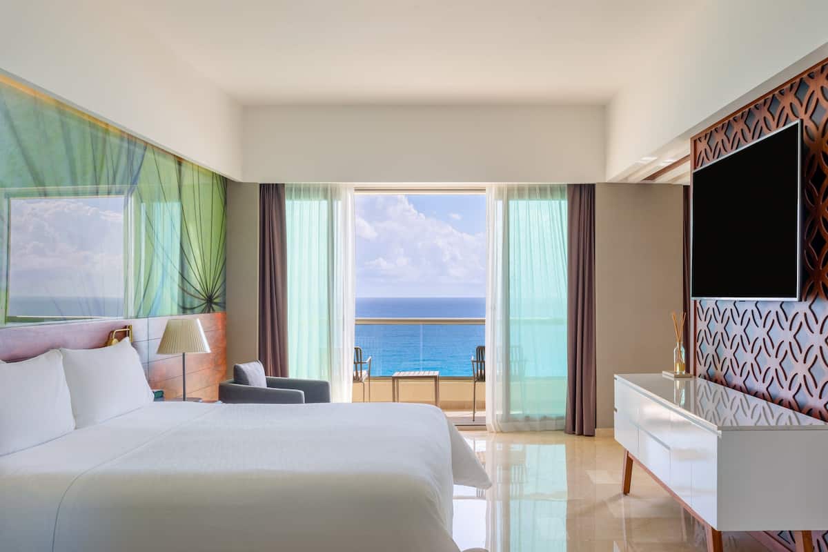 Ein Hotelzimmer mit einem großen Bett, einem Fernseher, einem Balkon mit Meerblick und einem modernen Design.