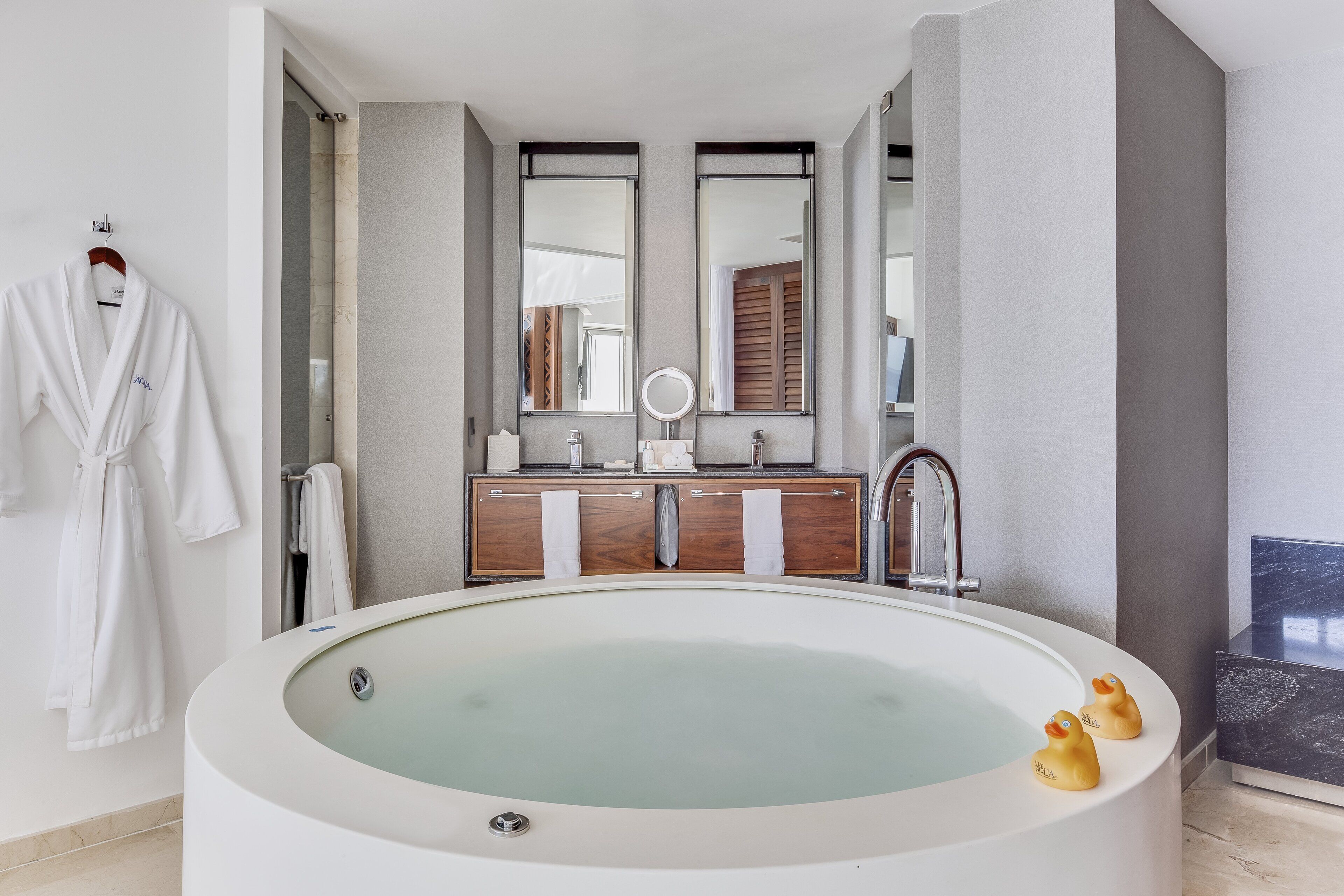 A modern bathroom with a large oval bathtub, a wooden vanity with a mirror, and two rubber ducks.