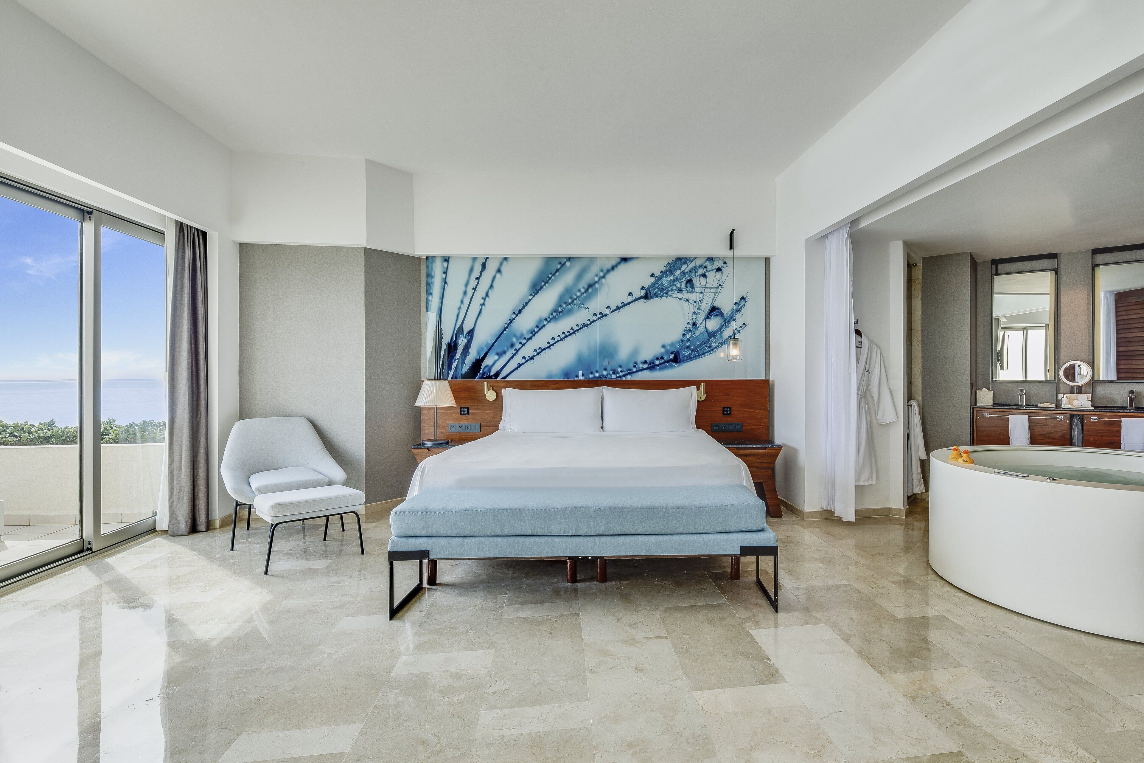 Una habitación de hotel moderna con una cama grande, un área de descanso, un baño y vistas al exterior.