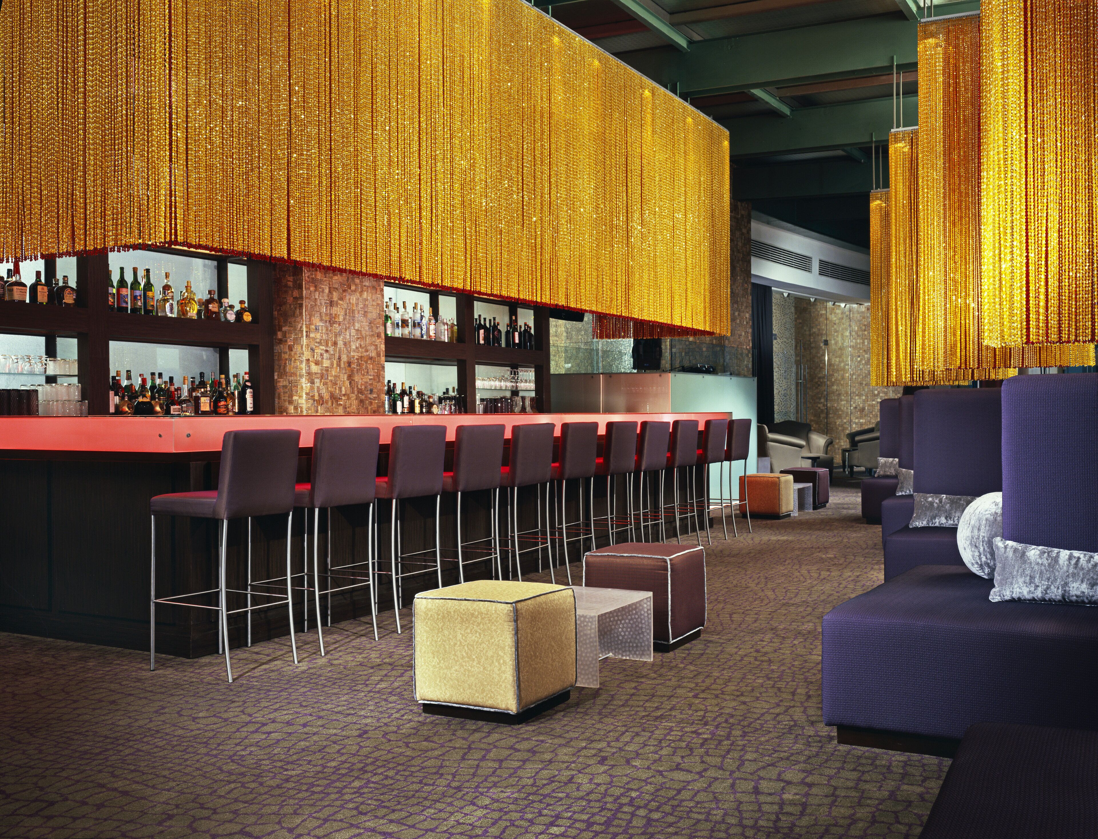 A bar area with a long counter, multiple bar stools, and a seating area with sofas and ottomans.