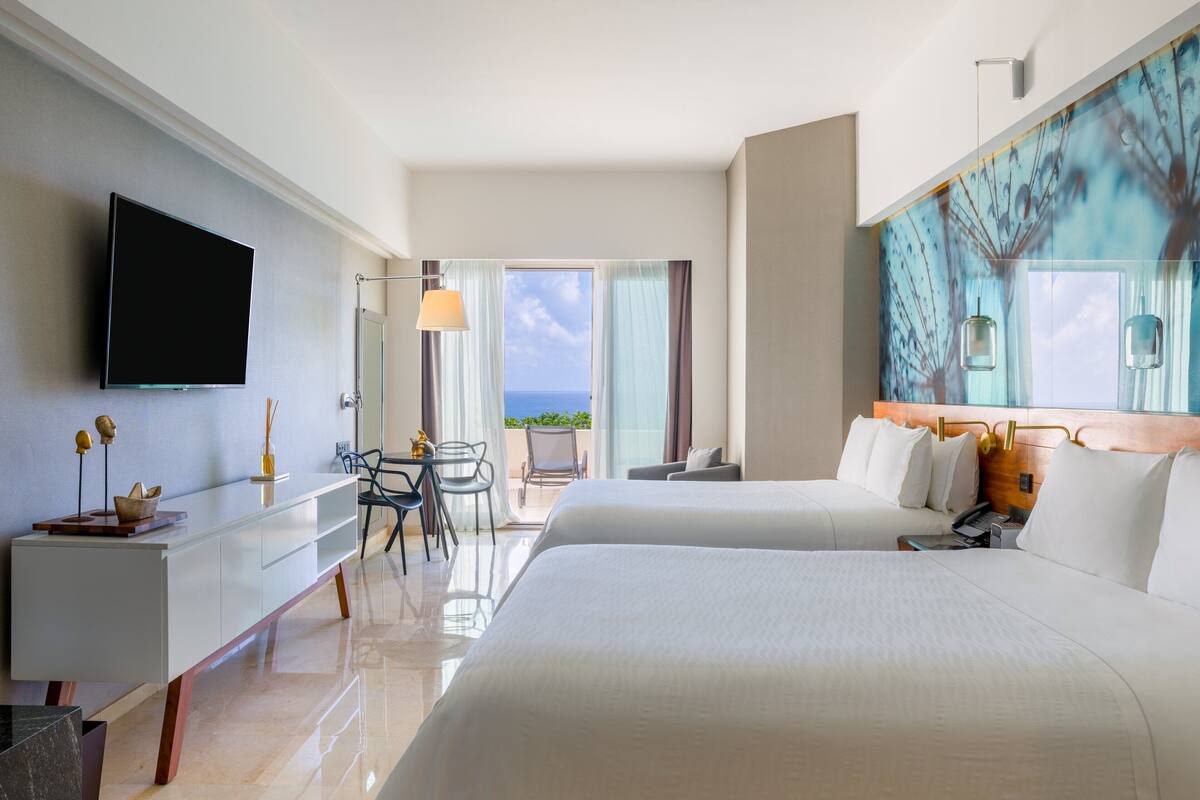 Ein Hotelzimmer mit zwei Betten, einem Schreibtisch, einem Sessel und Meerblick.