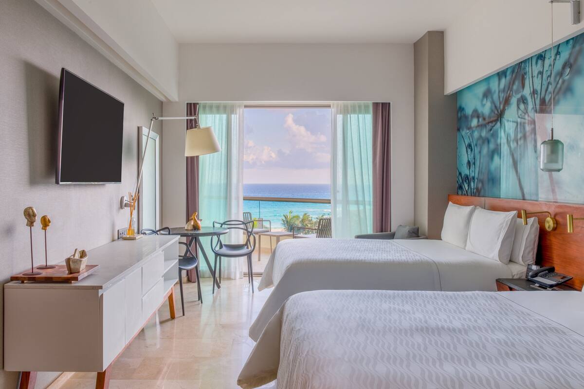 Ein Hotelzimmer mit zwei Betten, einem Schreibtisch, einem Fernseher und Meerblick.