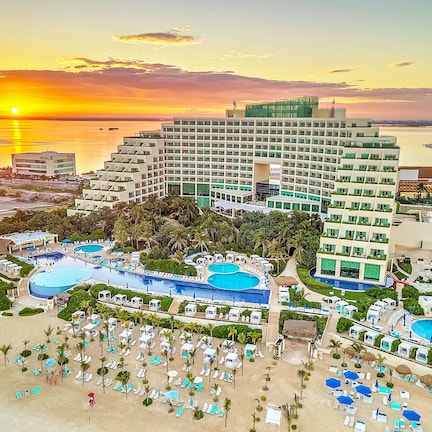 A resort with multiple swimming pools, a beach area with sun loungers, and a large building with a modern design.