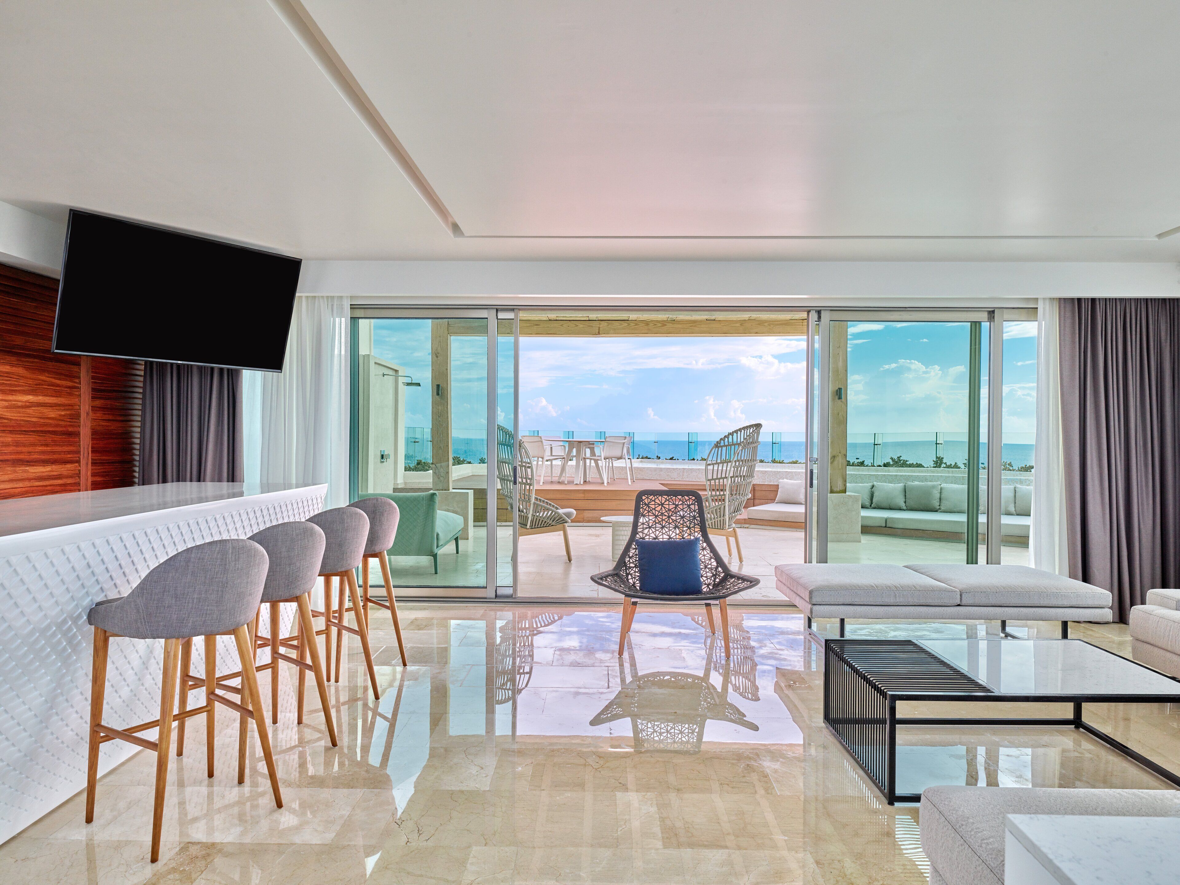 Una habitación de hotel moderna con balcón, zona de bar y un espacio de estar con vistas al océano.
