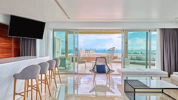 Una habitación de hotel moderna con balcón, zona de bar y un espacio de estar con vistas al océano.