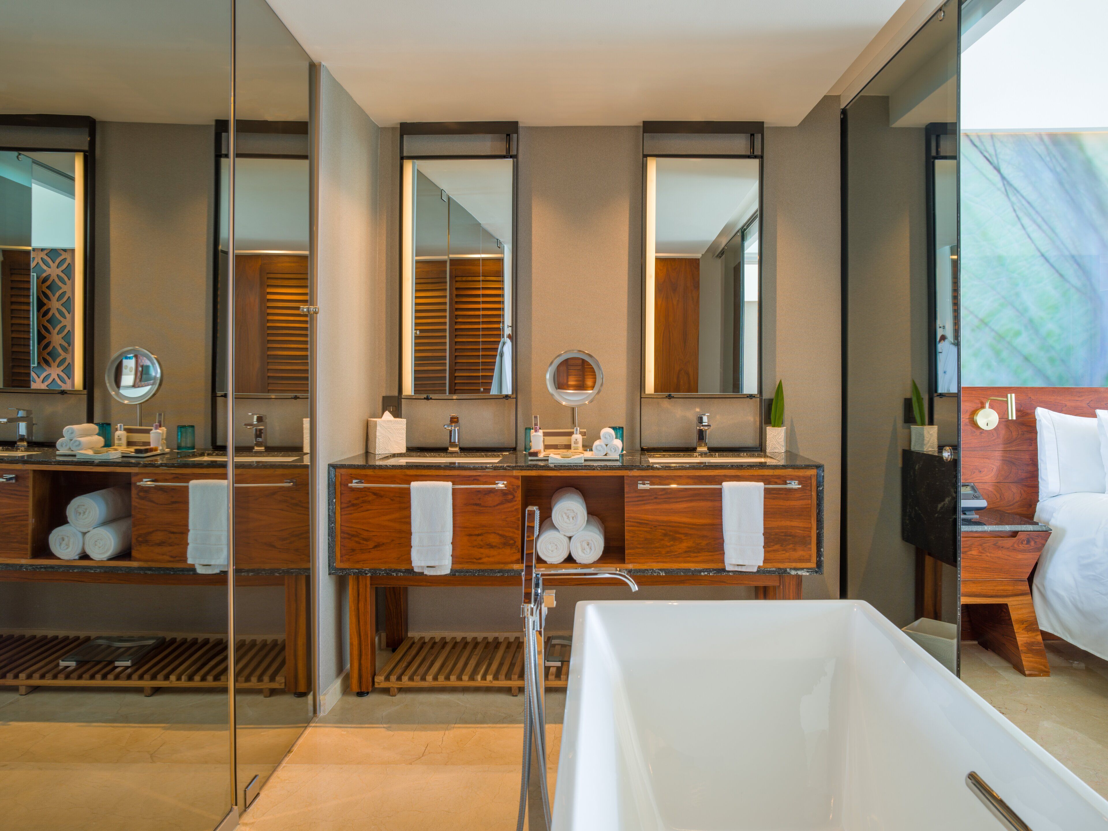Un baño moderno con dos lavamanos, espejos grandes, una bañera y muebles de madera.