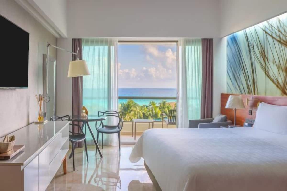 Ein Hotelzimmer mit Bett, Schreibtisch, Stuhl, Fernseher und einem Balkon mit Meerblick.