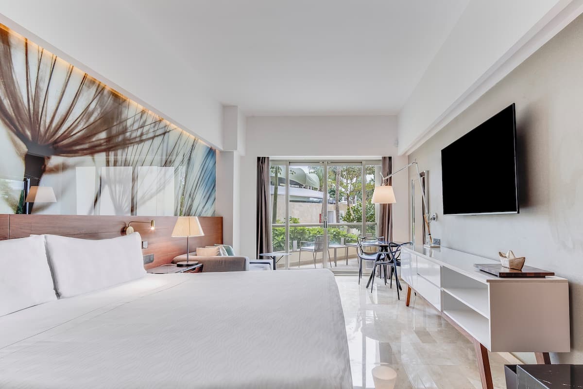 Ein modernes Hotelzimmer mit einem großen Bett, einem Schreibtisch mit Stuhl, einem Flachbildfernseher und einem Balkon mit Blick auf die Stadt.