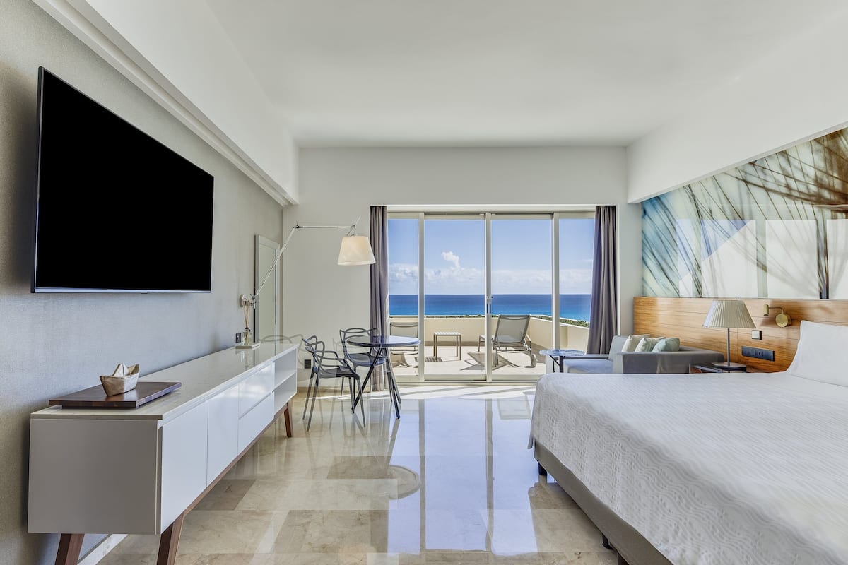 Ein modernes Hotelzimmer mit einem großen Bett, einem Flachbildfernseher, einem Schreibtisch und einem Balkon mit Meerblick.