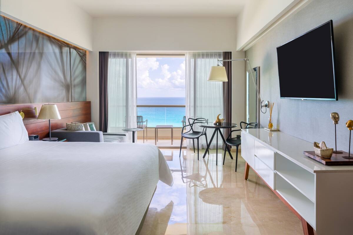 Ein Hotelzimmer mit einem Bett, einem Schreibtisch, einem Sessel, einem Fernseher und Blick aufs Meer.