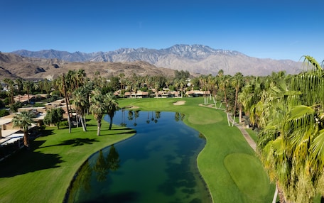 A golf course with a pond, palm trees, and mountains in the background.