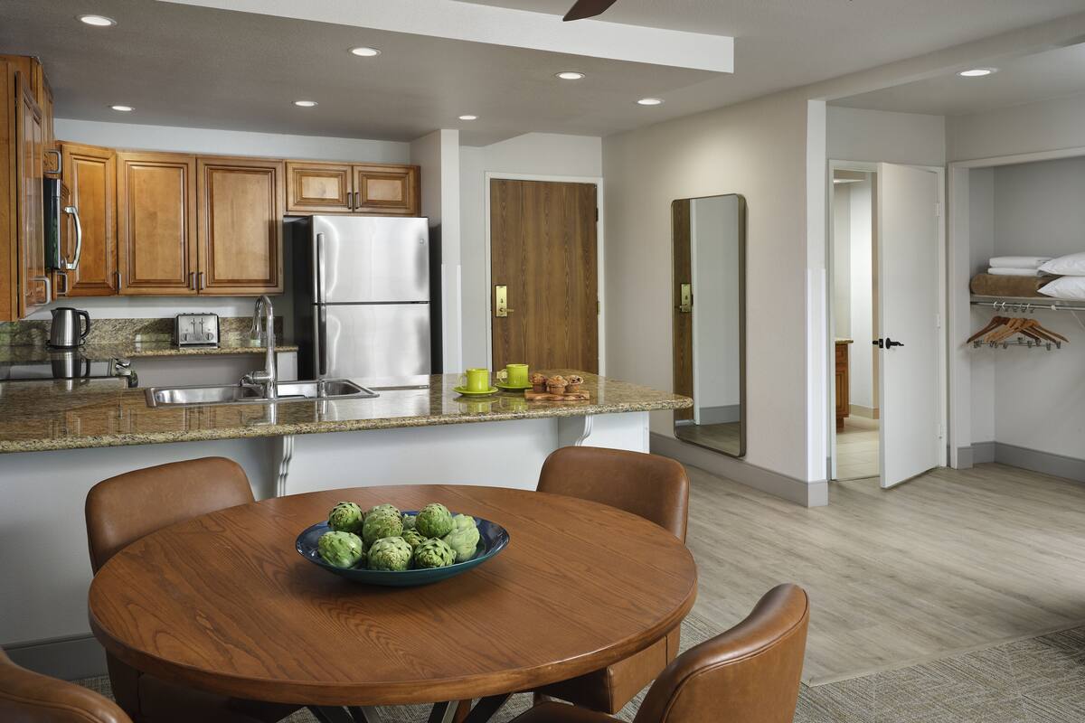 A modern kitchen with wooden cabinets, stainless steel appliances, and a dining area with a table and chairs.