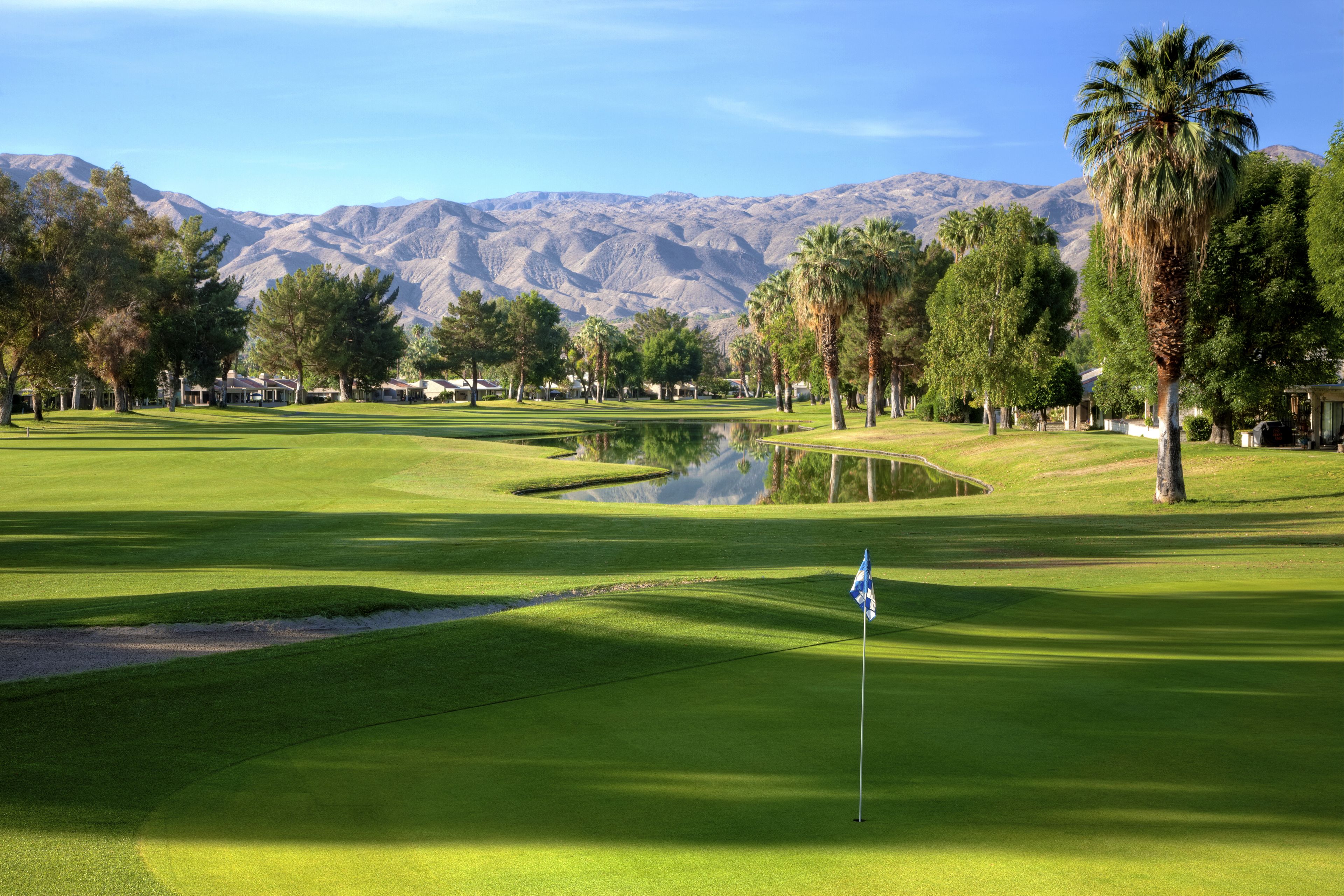 A golf course with a flagstick, water hazards, and a mountainous backdrop.